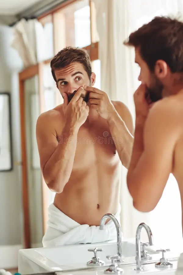 Man examining a pimple on his nose in a bathroom mirror — dermatology skin inspection concept